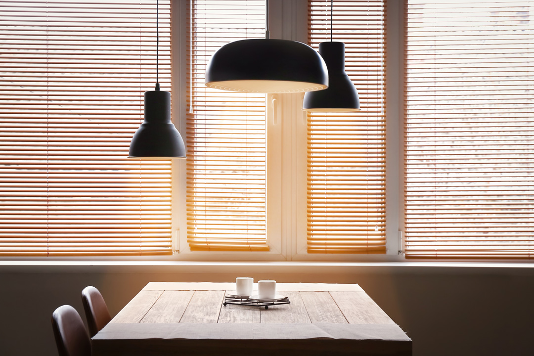 Timber venetian blinds installed in a modern living room with pendant lamps and dining table