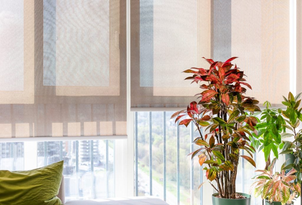 Beige roller blinds in a high-floor apartment gently filter sunlight through large windows