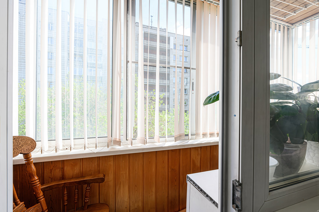 White vertical blinds on a bright balcony filtering sunlight with a city skyline view beyond
