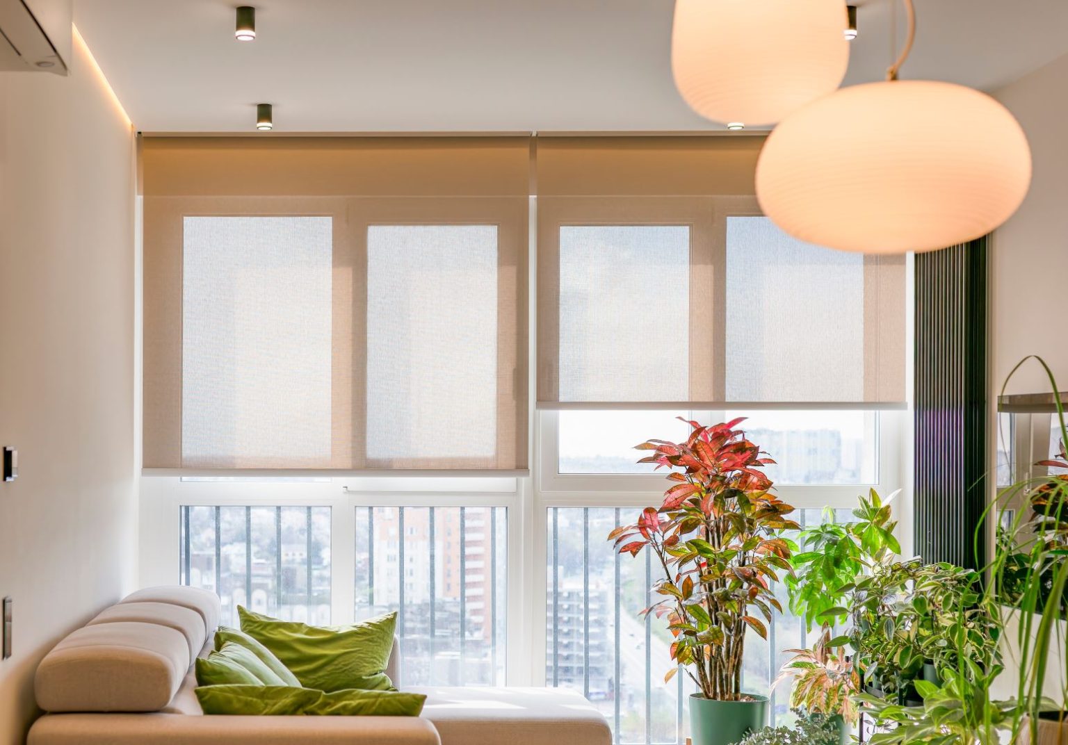 Living room with automatic roller blinds partially closed over large windows, allowing soft natural light to filter through