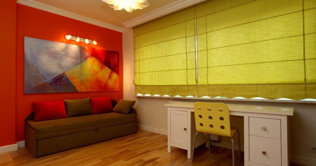 A large lime-green Roman shades covering a window above a white desk.