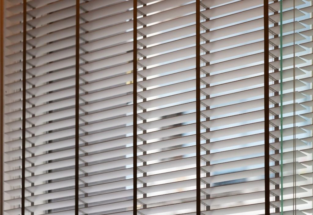 A close-up, angled view of white venetian blinds featuring dark brown or black decorative tapes