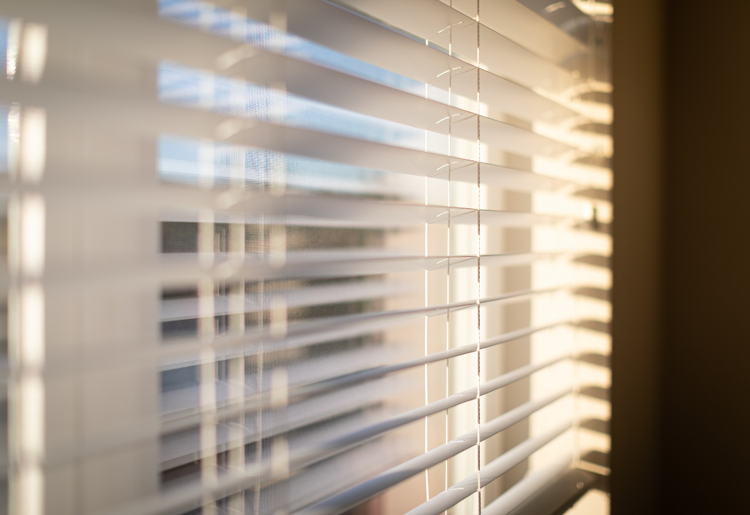 A close-up, angled view of dark wooden horizontal blinds with a silhouette of a person on the left.