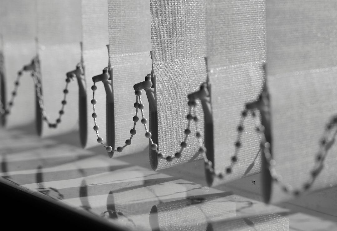 close-up shot of vertical blinds, showing the individual fabric slats and the beaded chains that control their angle.