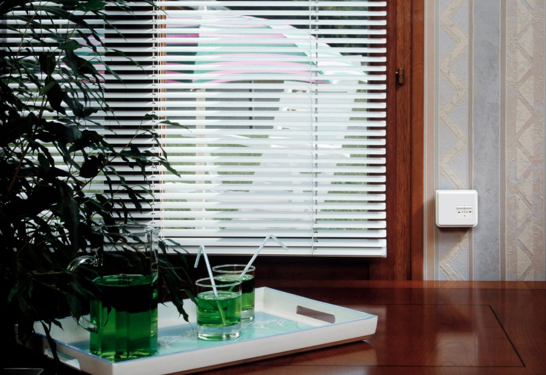 A close-up of a large window with white horizontal blinds that are partially open, allowing light to filter through.