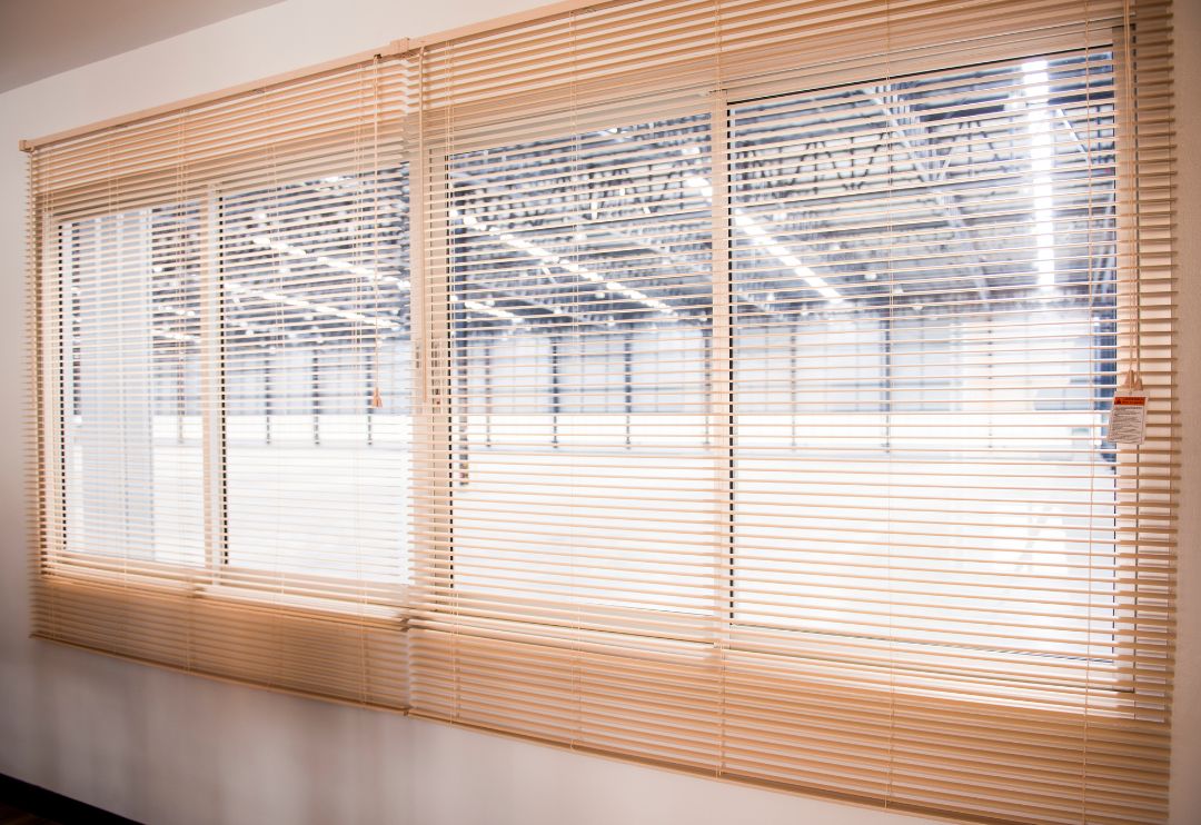 An angled wide shot of several large windows covered by light cream-coloured horizontal venetian blinds