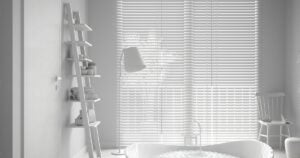 A minimalist, all-white bathroom featuring a freestanding tub, a ladder-style shelf, and a large window with white Venetian blinds that filter the silhouette of a palm tree.