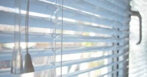 Close-up of thin white Venetian blinds with pull cords and a tilt wand.