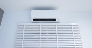 White split-system air conditioner mounted on a wall above closed white Venetian blinds.