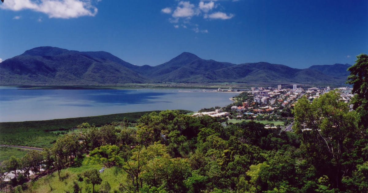 An elevated, wide-angle view of a coastal city nestled between lush green forests and a large blue bay.