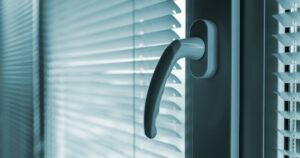 A close-up focusing on a curved, light-coloured window handle against a backdrop of partially open Venetian blinds.