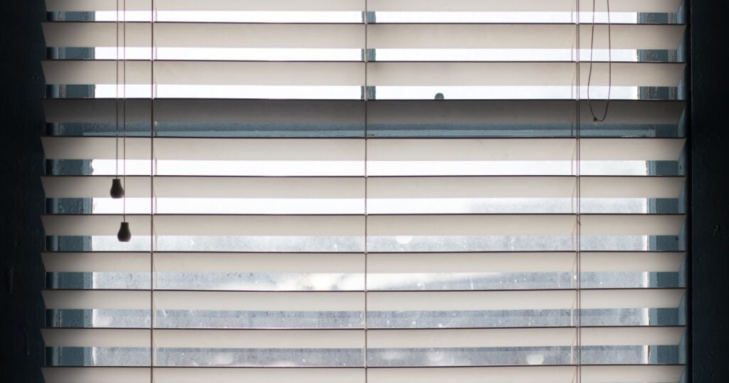 A straight-on view of white horizontal window blinds with pull cords