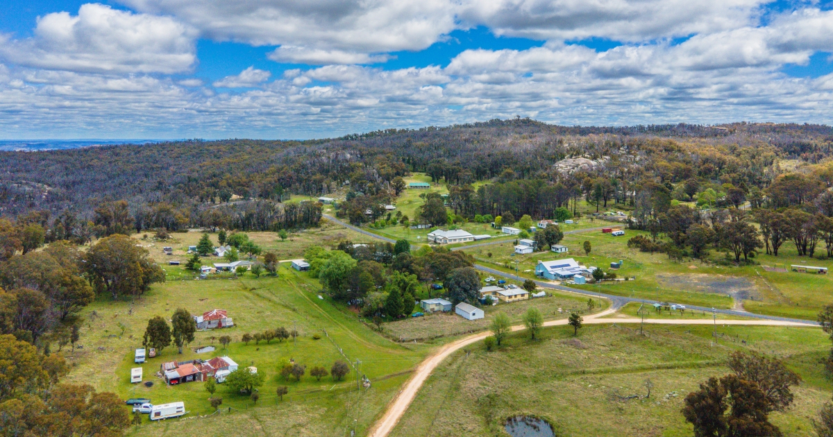 An expansive aerial view of a rural town nestled in a valley with rolling green fields, scattered houses, and dense forest