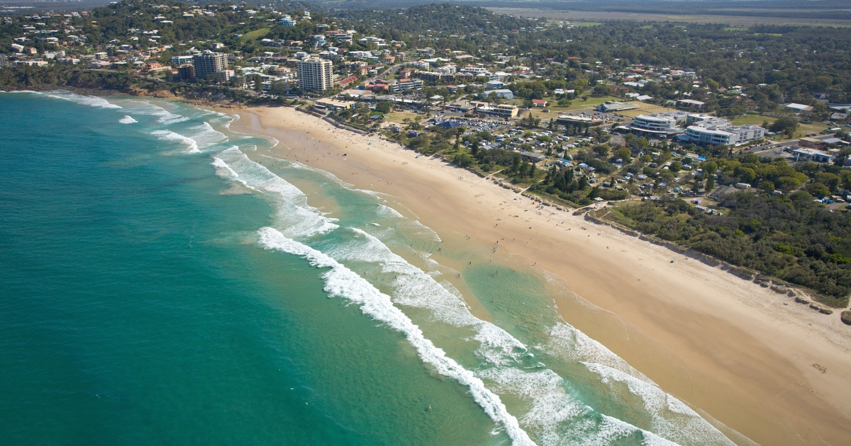 An aerial, wide-angle view of a long, sandy beach meeting turquoise ocean waves