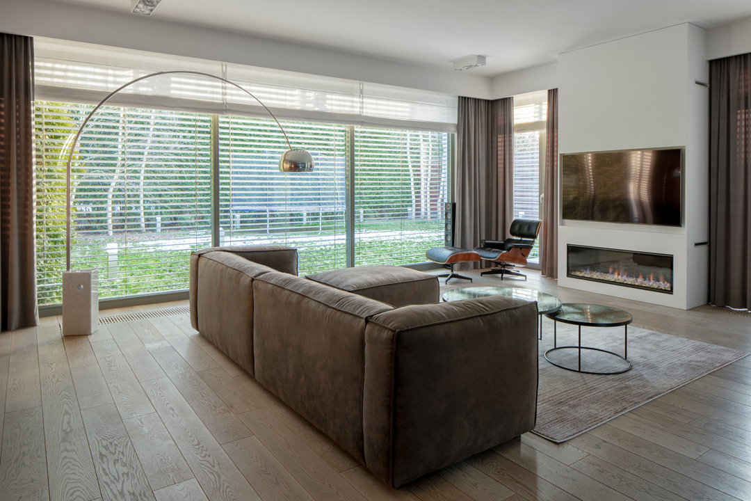 Luxury and stylish living room with window wall, window blinds, elegant furniture and television and modern fireplace in wall