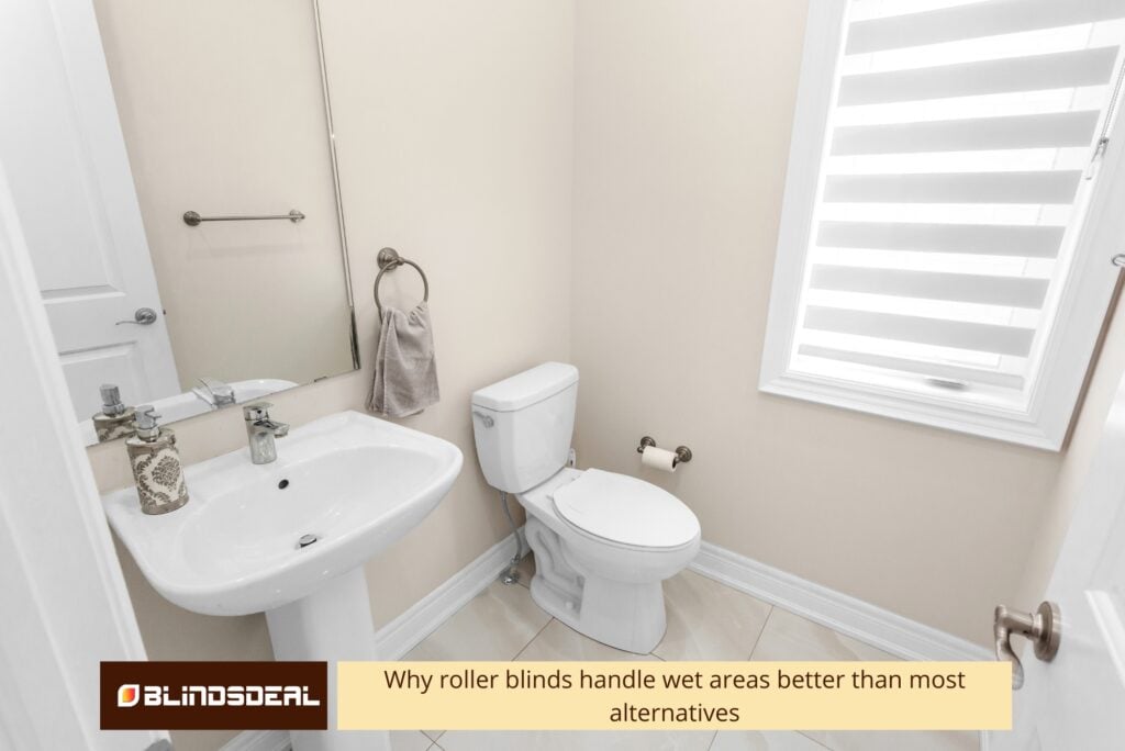 Brightly lit bathroom featuring a white pedestal sink, toilet, and a window fitted with white zebra-style roller blinds.