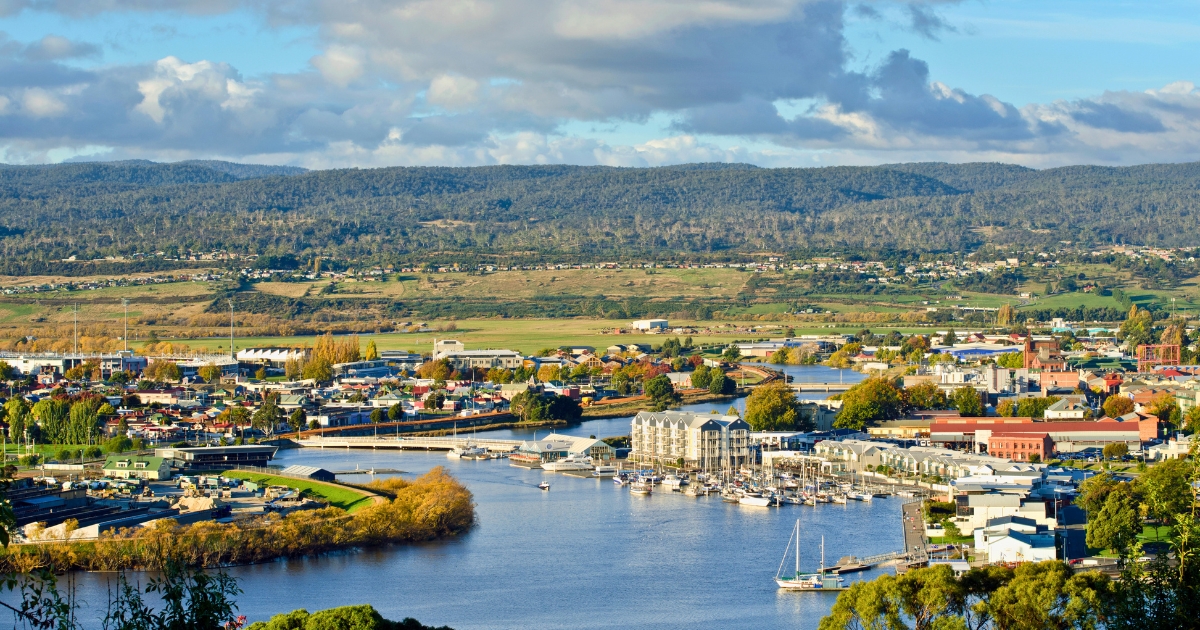 A coastal town with buildings along a wide river filled with boats and yachts, backed by rolling hills and a cloudy sky in Launceston.
