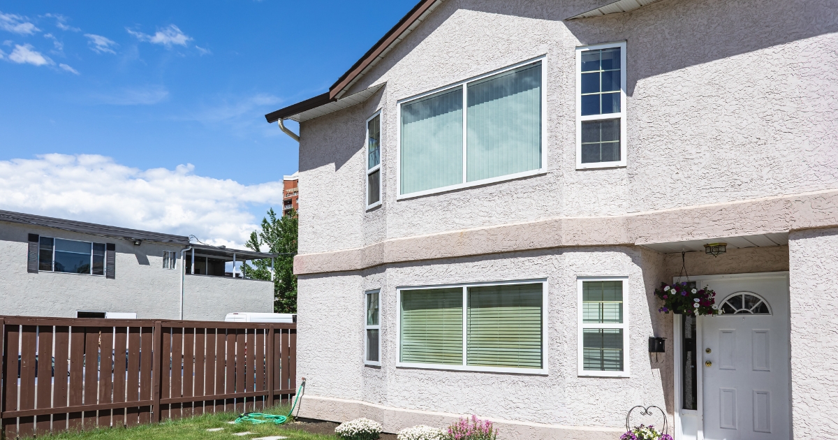 A two-storey beige house featuring large windows with vertical blinds upstairs and horizontal Venetian blinds downstairs next to a white front door in Liverpool.